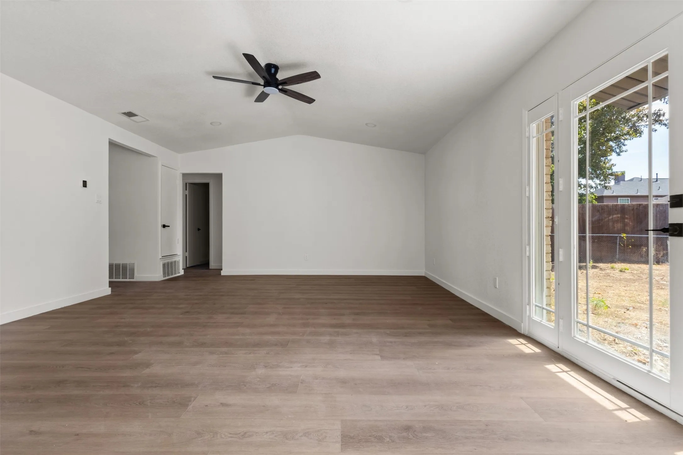 Vaulted ceiling, wood-finish flooring, ceiling fan, and double French doors with transom windows
