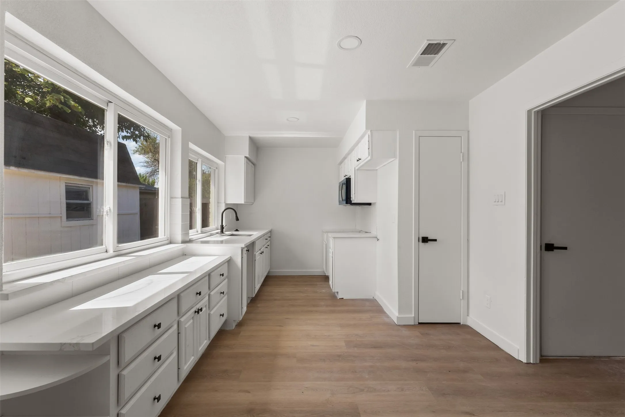 Contemporary kitchen with wood-finish flooring, white cabinetry, integrated sink, and black hardware