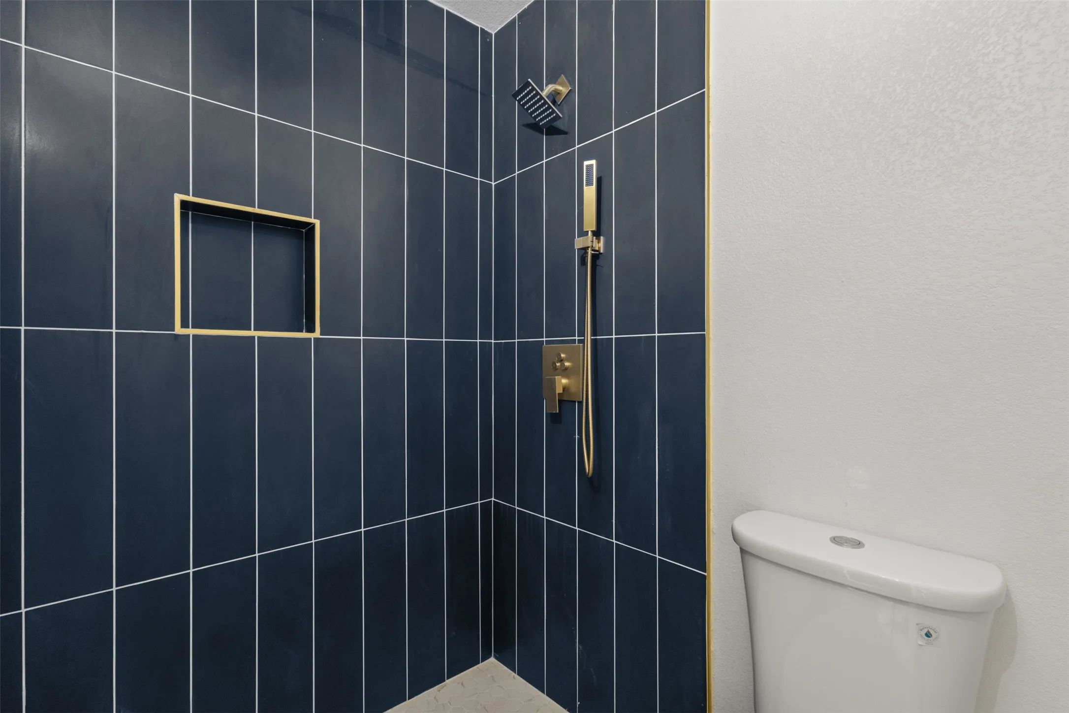 Shower stall with vertical dark blue tile, integrated niche, and gold-finish fixtures
