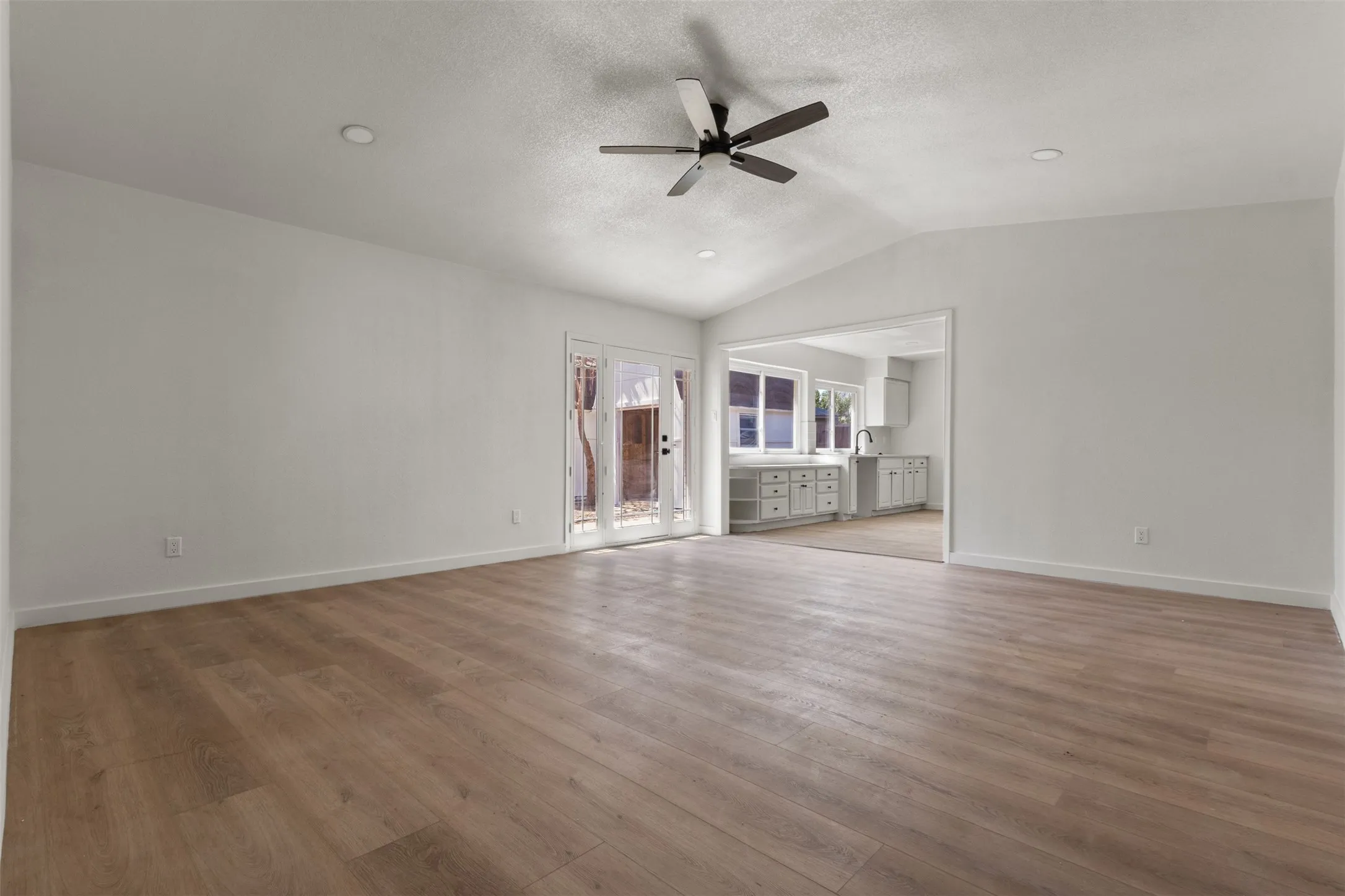 Vaulted ceiling with a ceiling fan, recessed lighting, wood-finish flooring, and French doors