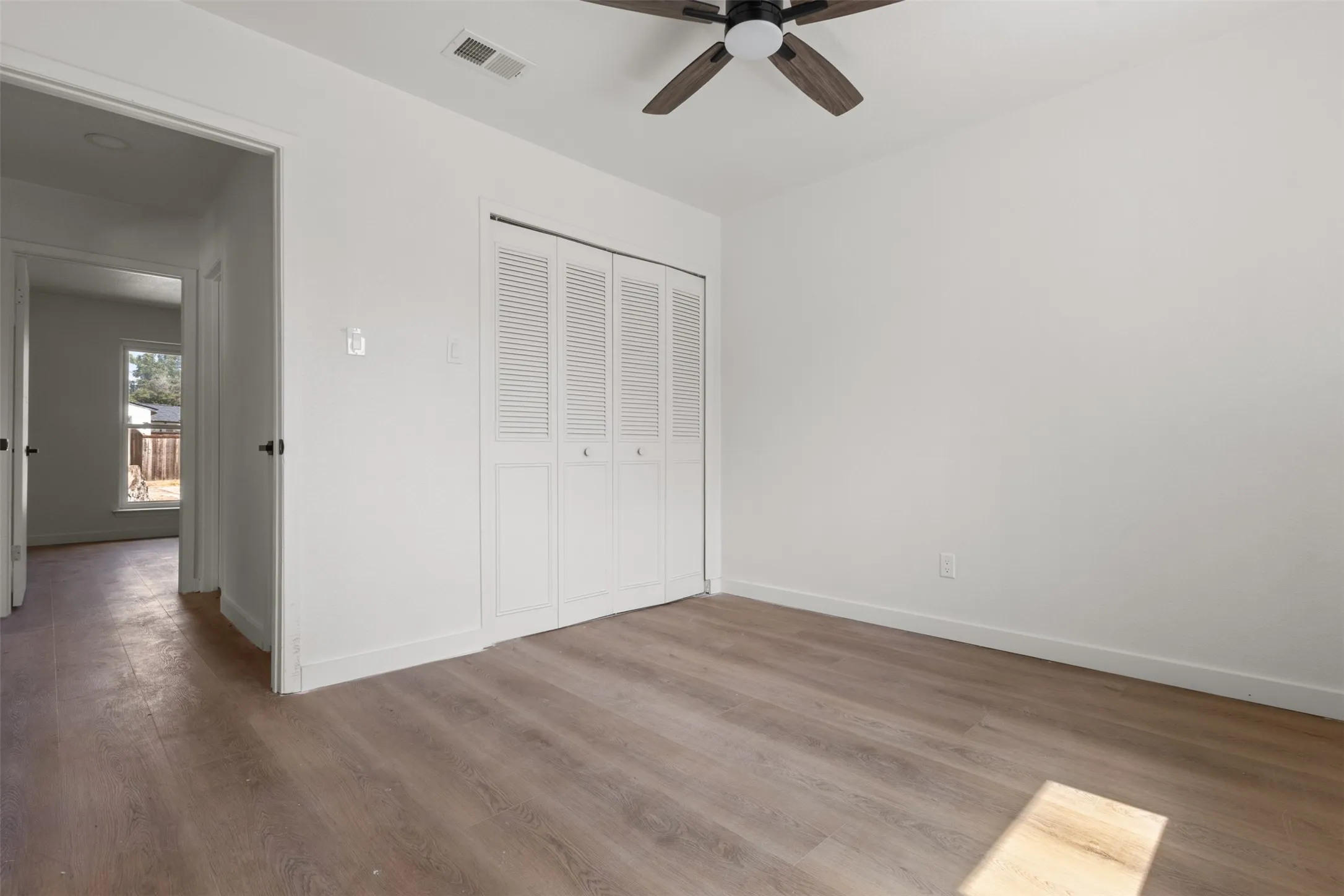Wood-finish flooring throughout, white walls, louvered bi-fold closet doors, and a ceiling fan with light fixture