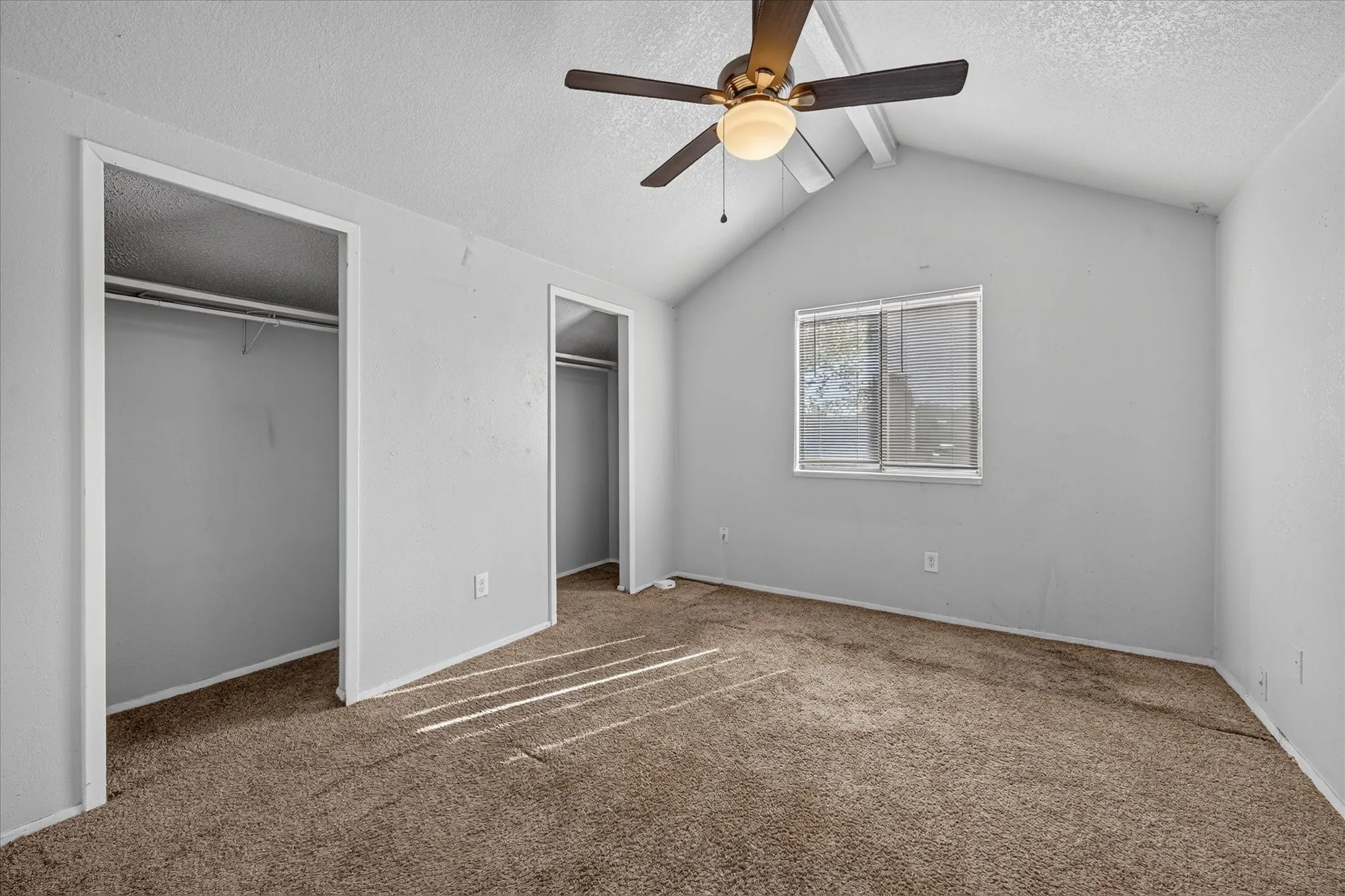 Vaulted ceiling with an integrated ceiling fan, light gray wall finish, and two closet openings with built-in shelving and hanging rods
