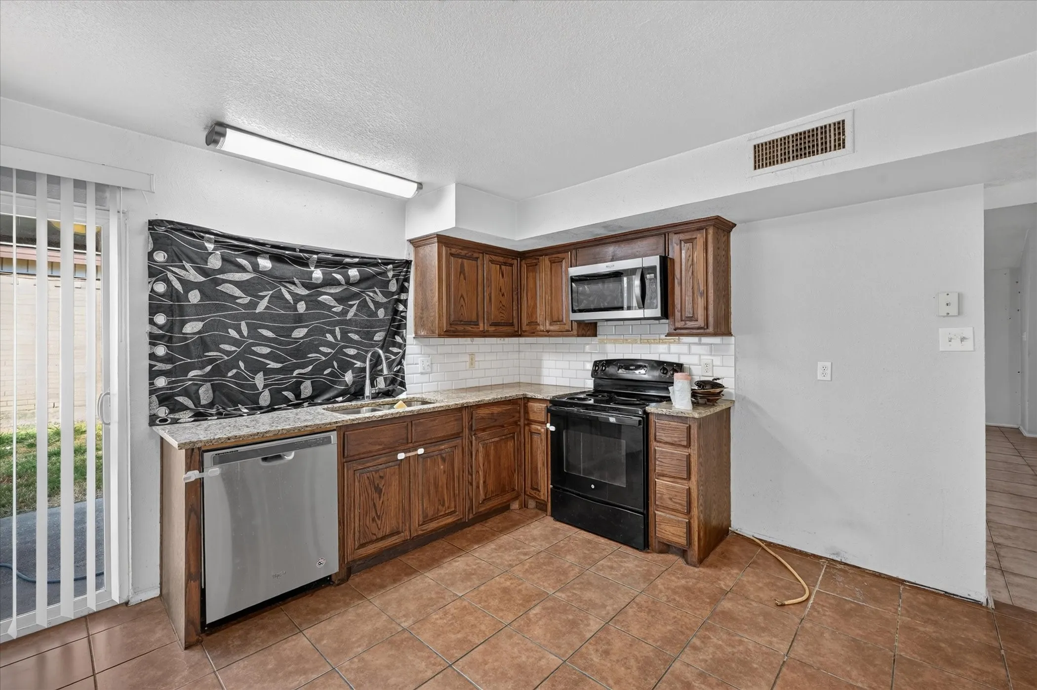 Kitchen featuring wood cabinetry, a stainless steel dishwasher, tile flooring, and a sliding glass door