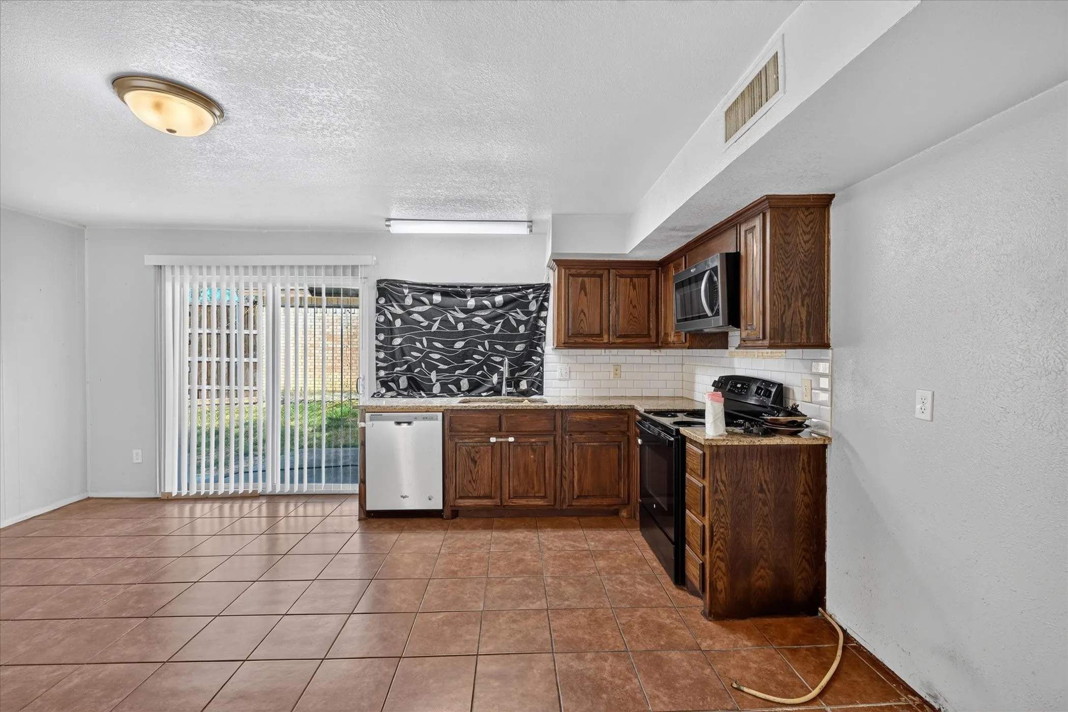 Kitchen with wood-finish cabinetry, white subway tile backsplash, and dark countertops
