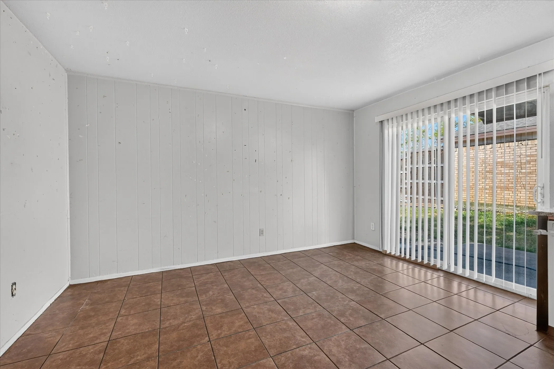 Tile flooring, vertical paneling accent wall, and a sliding glass door with vertical blinds