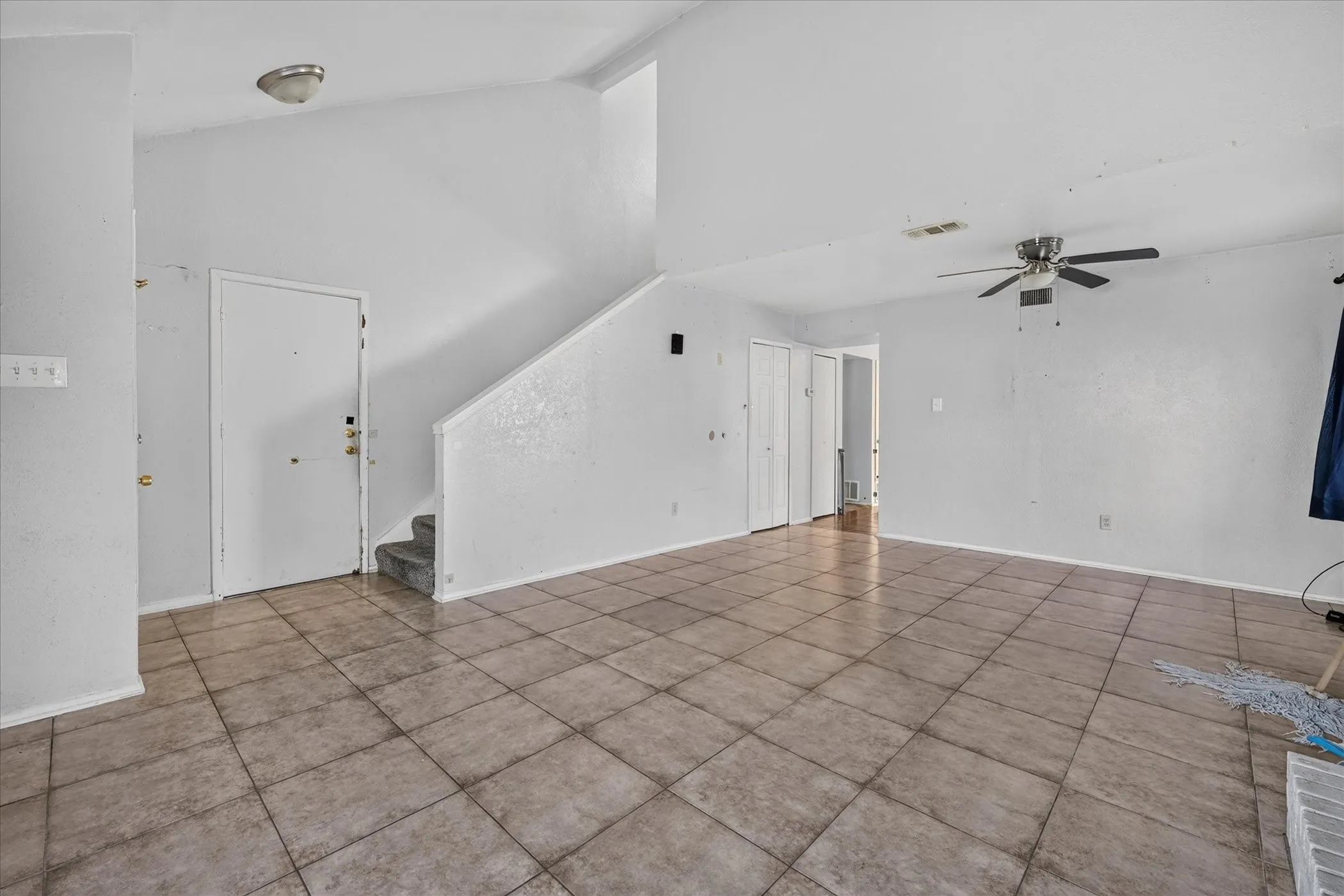 Vaulted ceiling, ceiling fan, tile flooring, interior staircase with carpeted steps, and white interior doors
