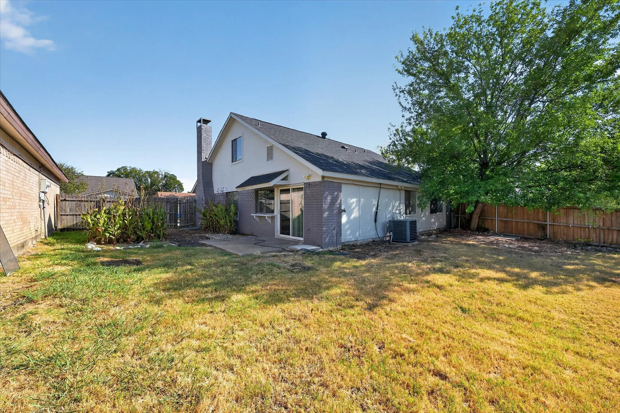 Expansive backyard featuring a mature tree, wood fencing, and a concrete patio