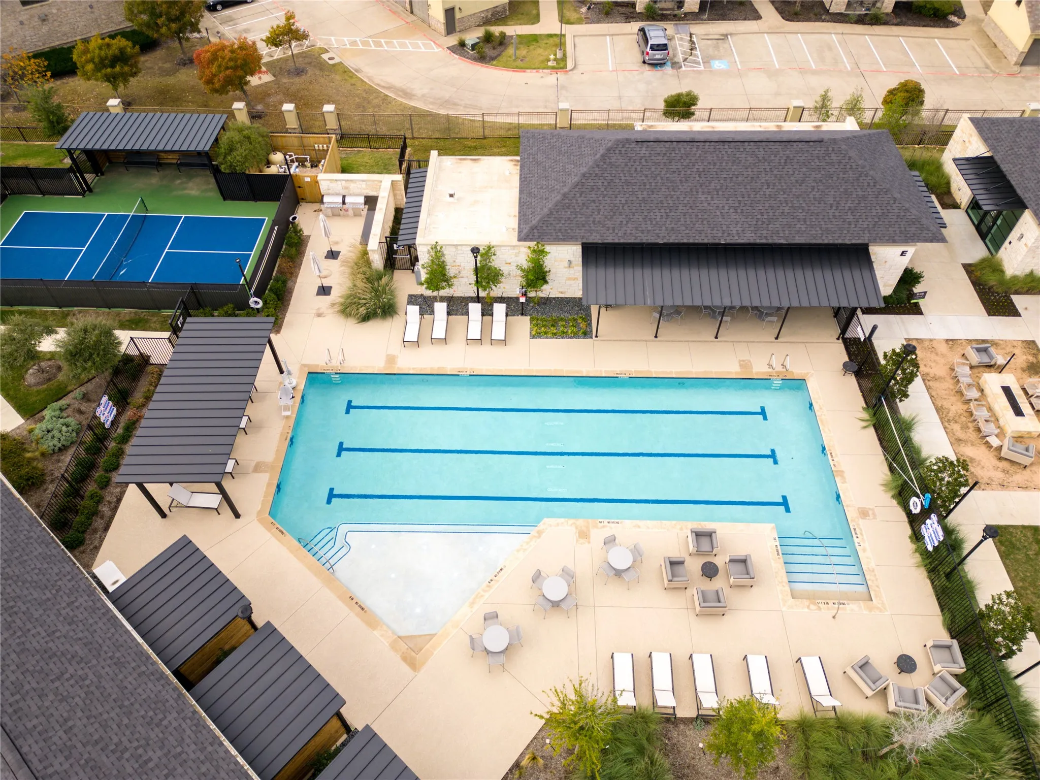 Resort-style pool with integrated steps, pickleball court, shaded lounge areas, and a fire pit feature