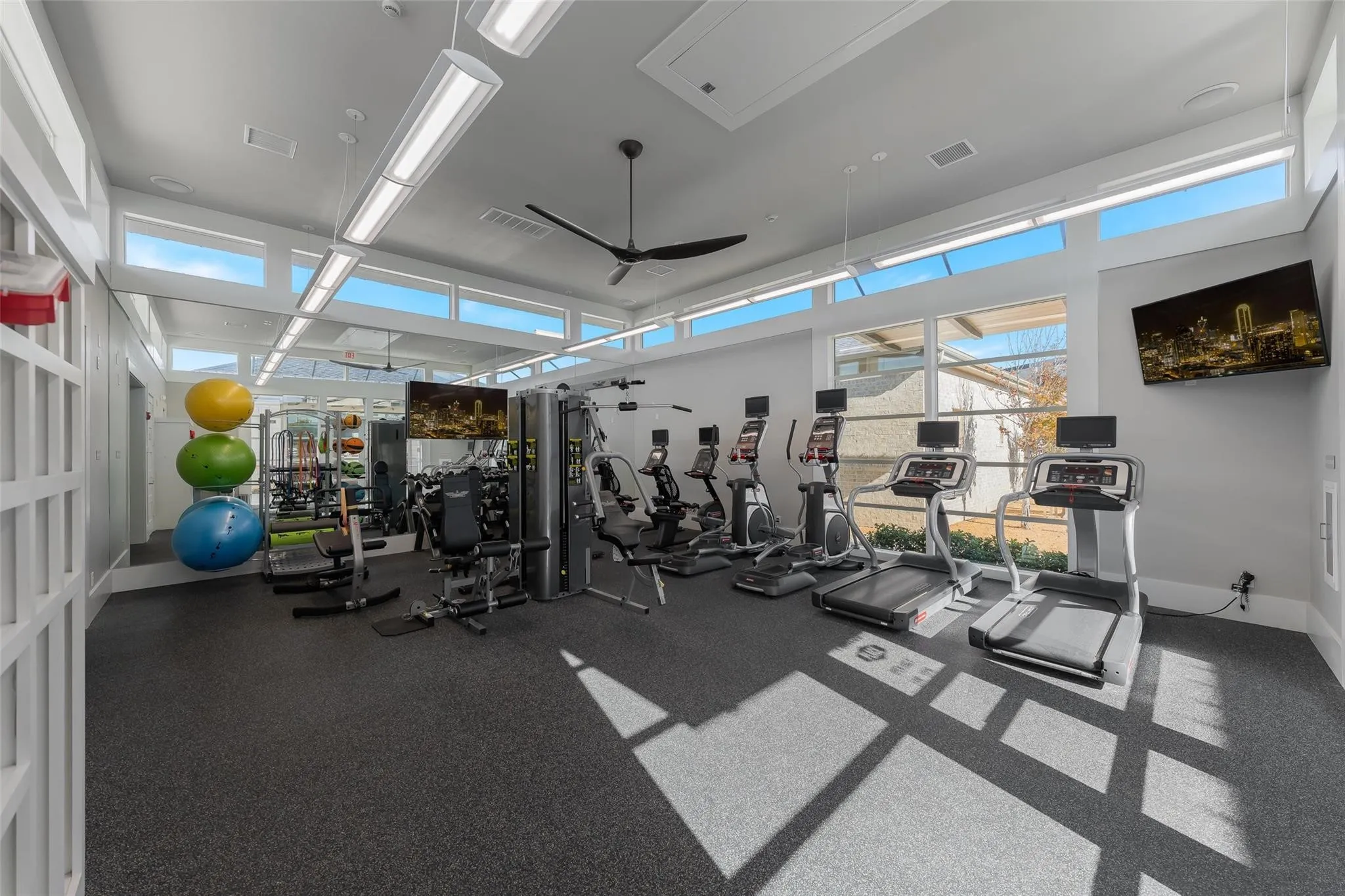 Fitness center featuring large windows, high ceilings, ceiling fan, and wall-mounted televisions