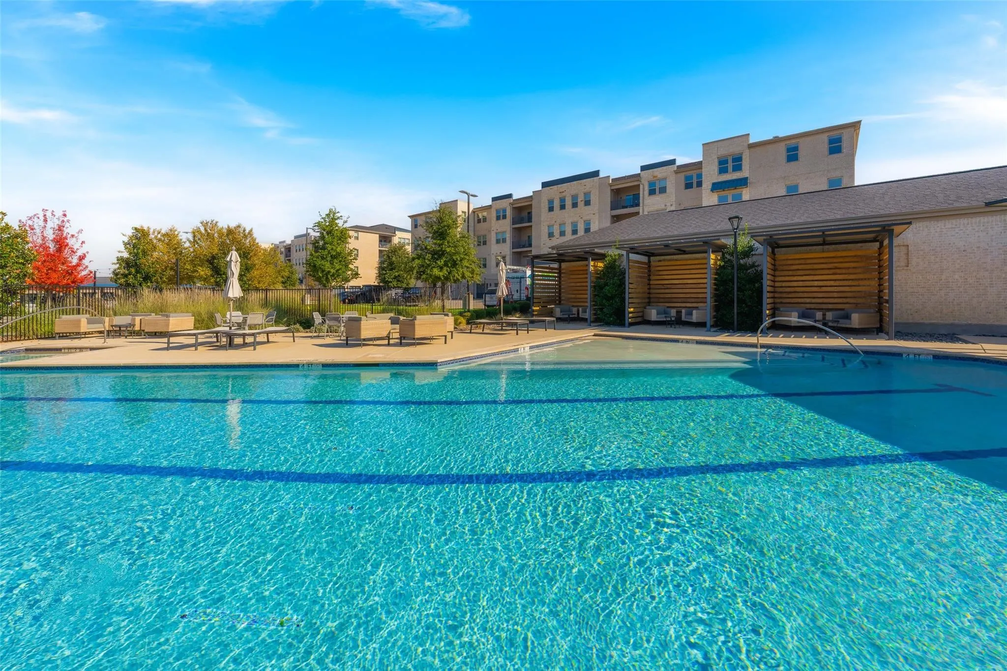 Outdoor swimming pool with integrated lounge seating, wood-slat cabanas, and surrounding paved deck