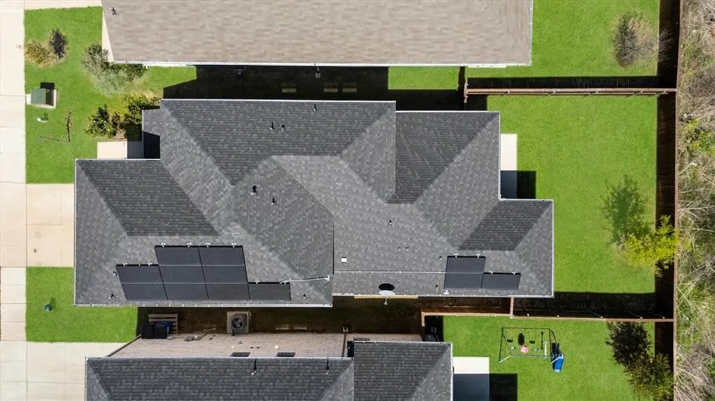 Expansive property featuring a dark shingle roof, solar panel installation, a concrete patio, and a fenced backyard with a manicured lawn