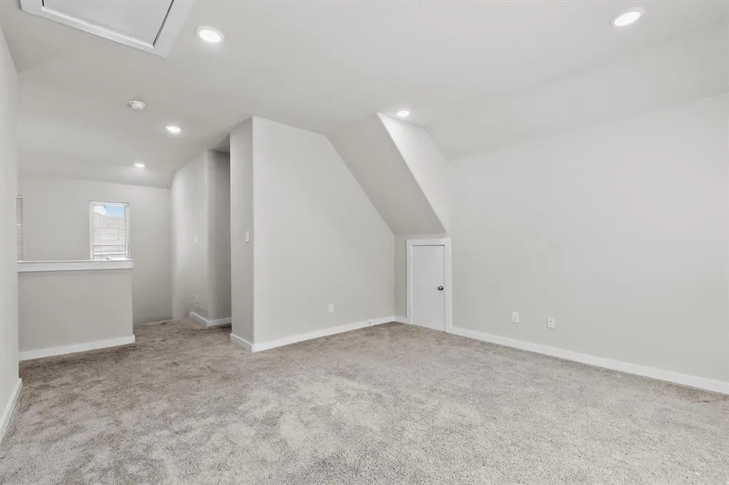 Recessed lighting illuminates this carpeted room with multiple wall surfaces and a window with blinds