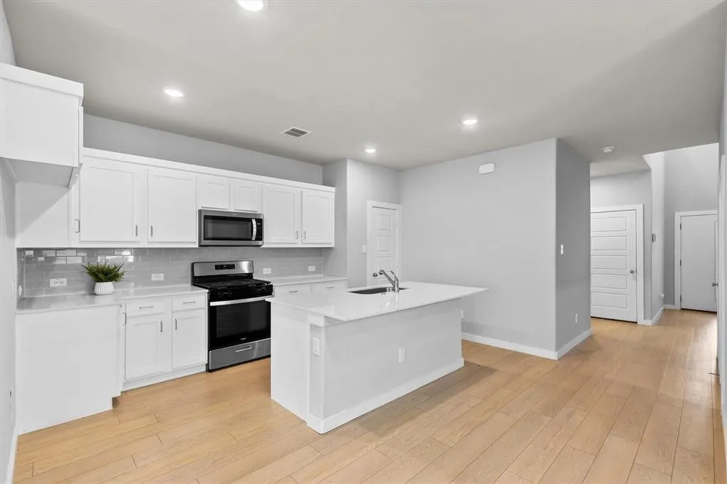 Kitchen featuring white shaker cabinetry, stainless steel appliances, light-toned wood-finish flooring, a kitchen island with an integrated sink, and recessed lighting