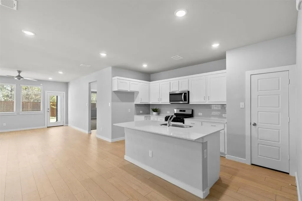 Wood-finish flooring throughout, recessed lighting, white shaker cabinetry, stainless steel appliances, and a kitchen island with a sink