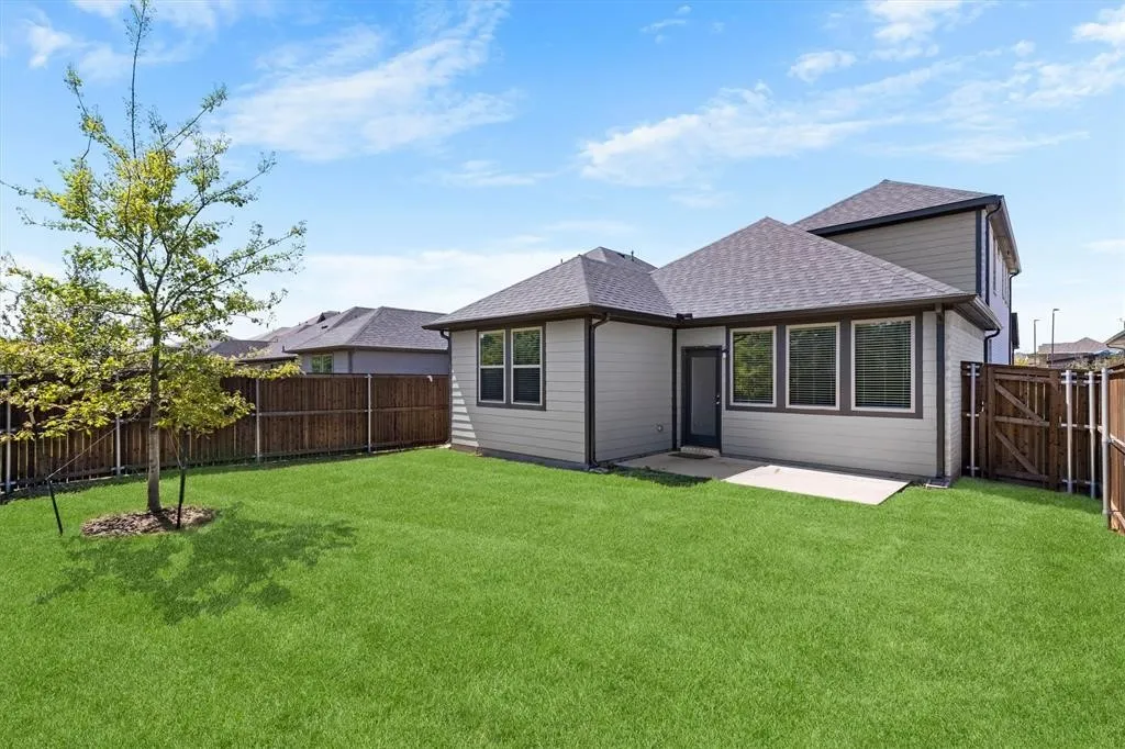 Expansive green lawn with a young tree, concrete patio, and dark wood privacy fencing