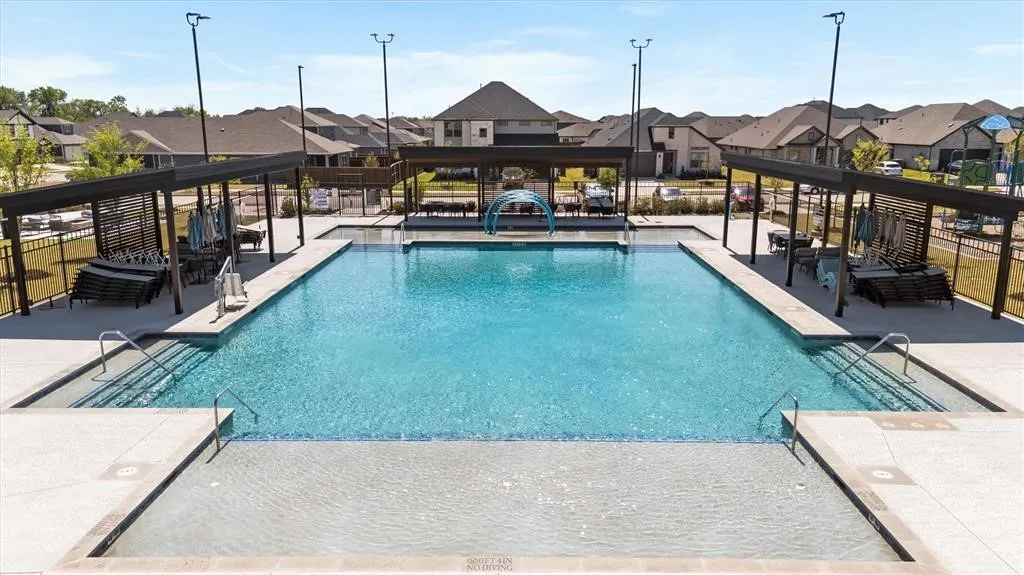 Expansive outdoor swimming pool with integrated shallow entry, shaded lounge areas, and surrounding concrete decking
