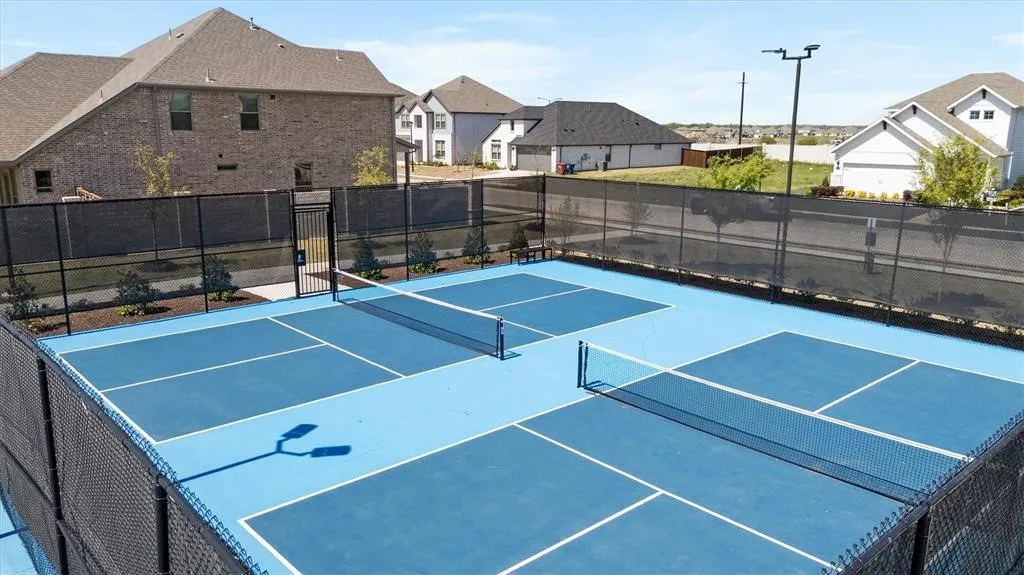 Four blue hard-surface courts, black perimeter fencing, and two court nets