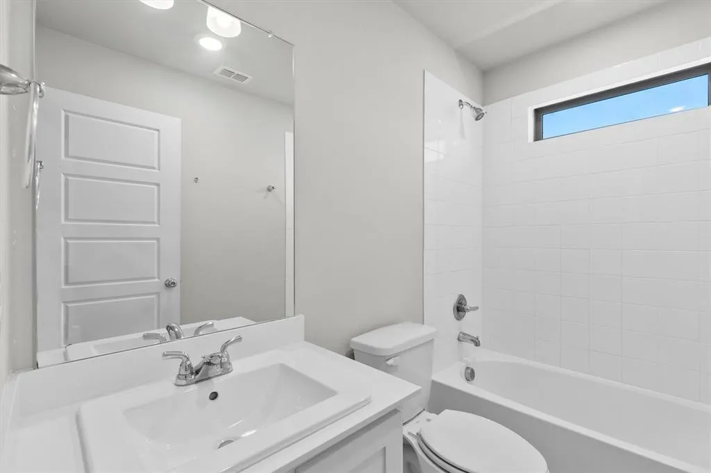 White vanity with integrated sink, chrome faucet, wall-mounted mirror, white subway tile tub surround, and a high horizontal window