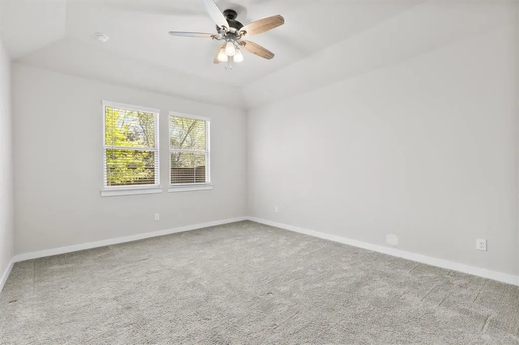Vaulted ceiling with a ceiling fan, two windows, wall-to-wall carpeting, and neutral wall tones