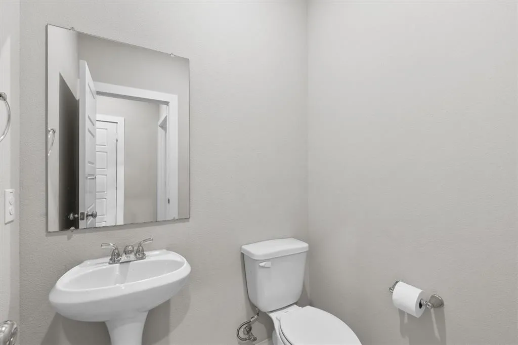 Pedestal sink with chrome faucet, wall-mounted mirror, and white toilet