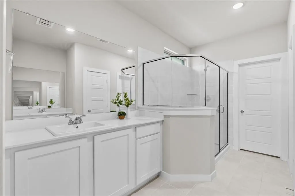 Dual vanity with integrated sinks, expansive wall mirror, walk-in shower with glass enclosure, tiled flooring, and modern panel doors
