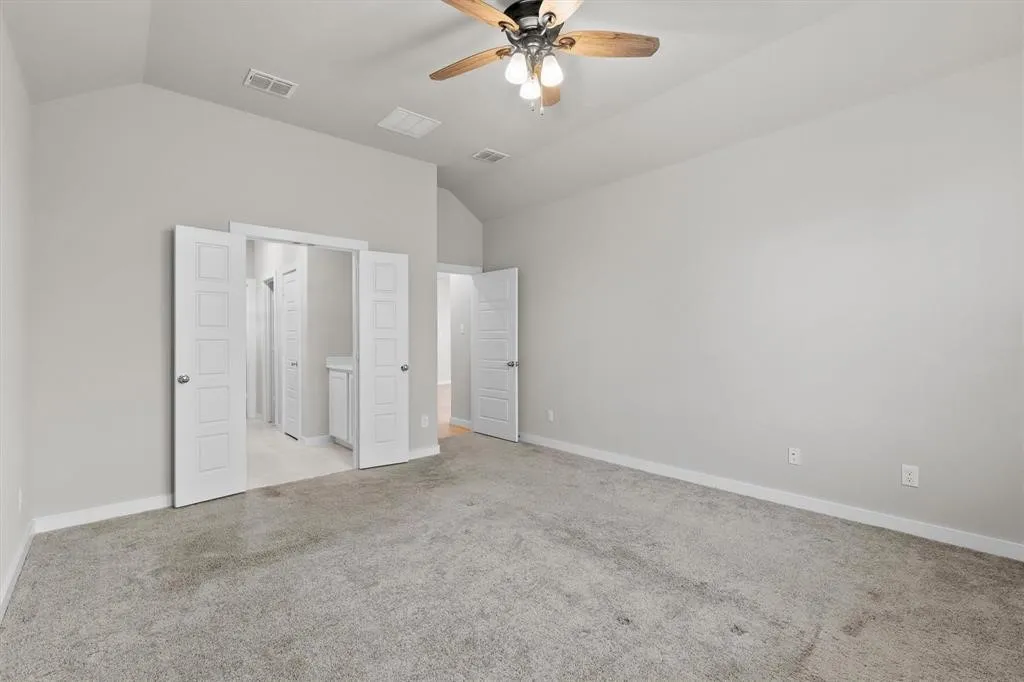 Vaulted ceiling with a wood-finish ceiling fan, neutral wall paint, and gray carpeted flooring