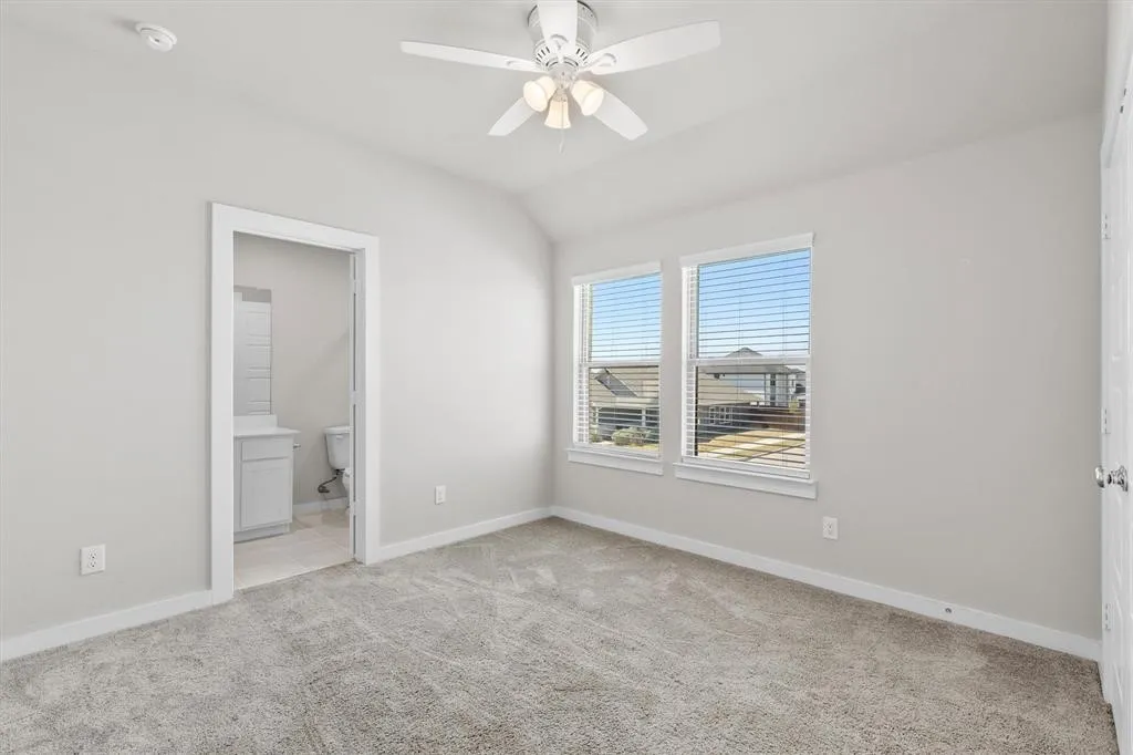 Vaulted ceiling with a ceiling fan light fixture, two windows with blinds, and carpet flooring