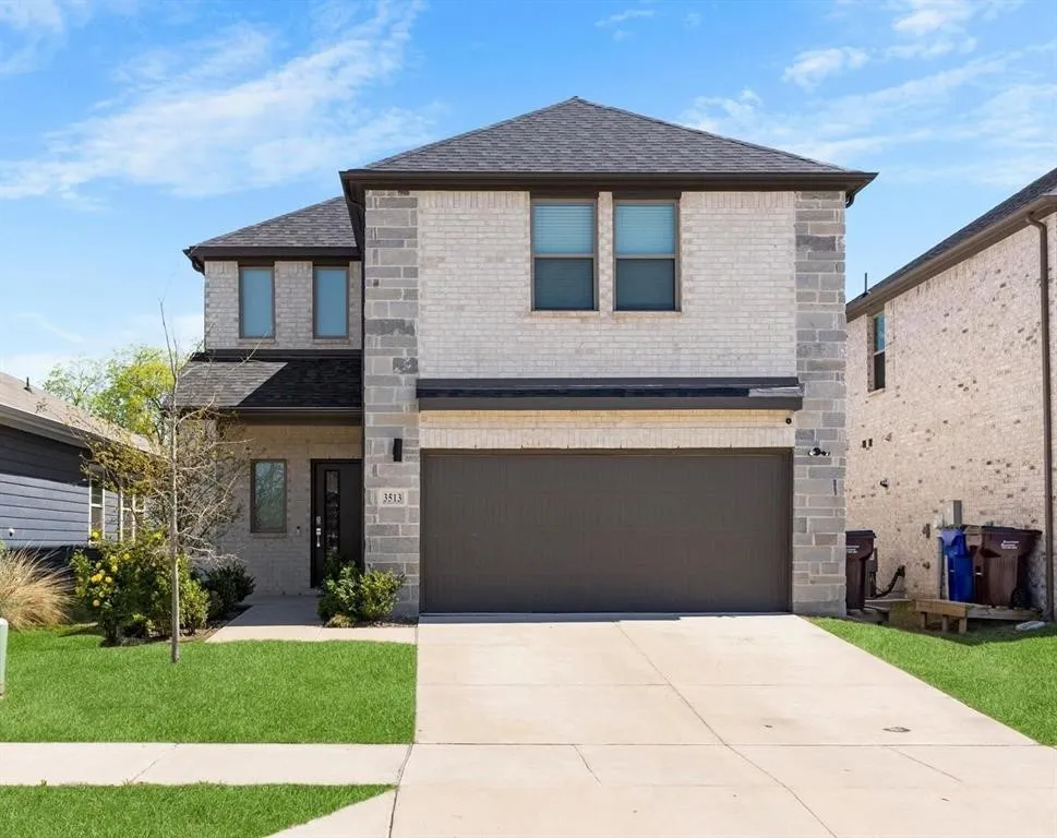 Two-story home with a light brick and stone facade, dark roof, attached garage, and concrete driveway