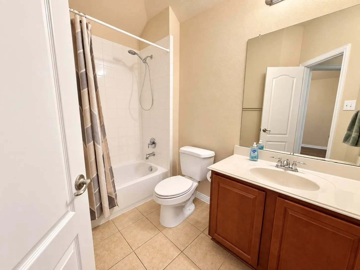 Bathroom with tile flooring, a built-in vanity featuring a single sink and wood-finish cabinetry, a toilet, and a shower-over-tub combination with tile surround