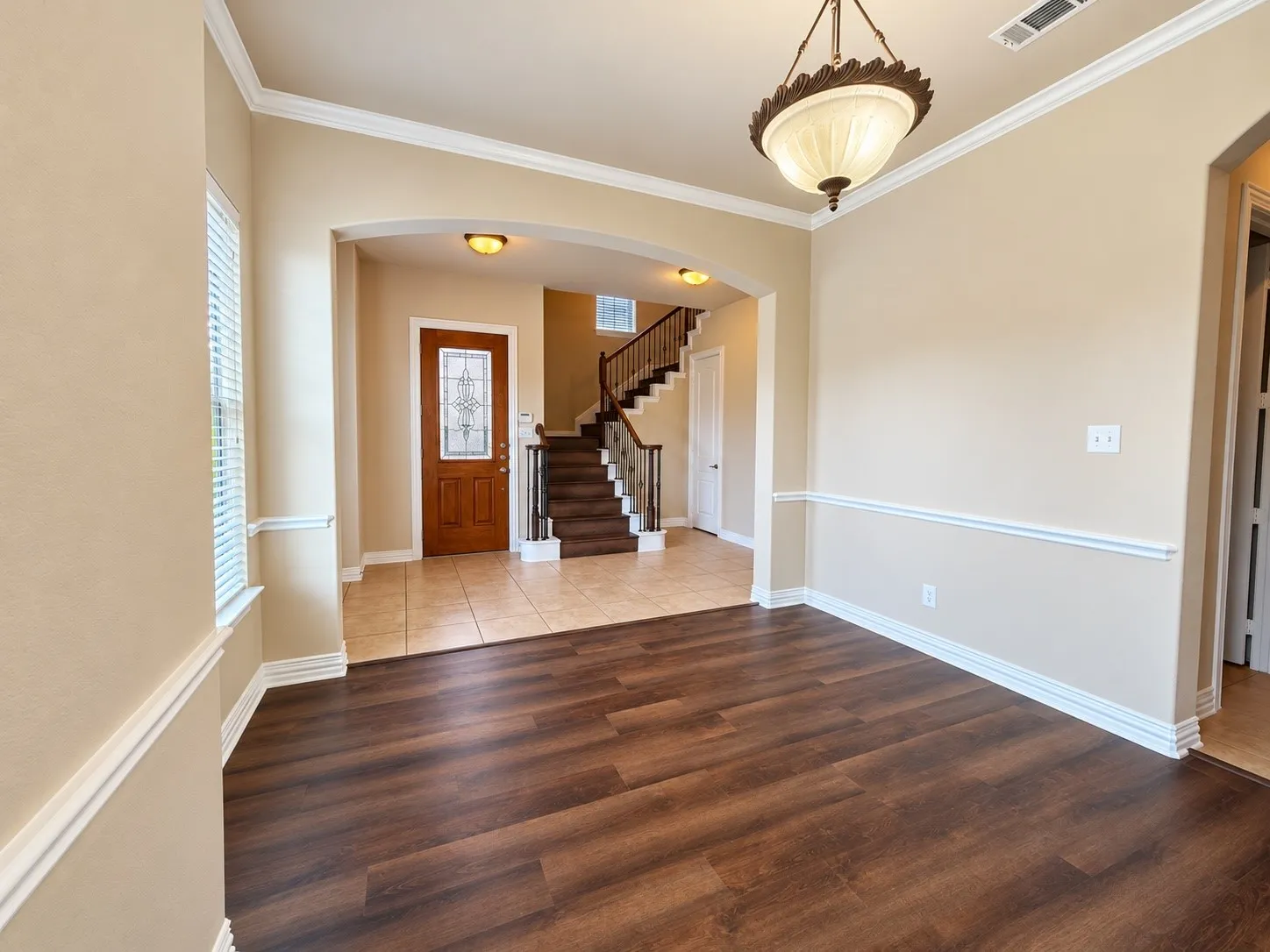 Wood-finish flooring, crown molding, chair rail molding, an arched entryway, and a decorative ceiling fixture