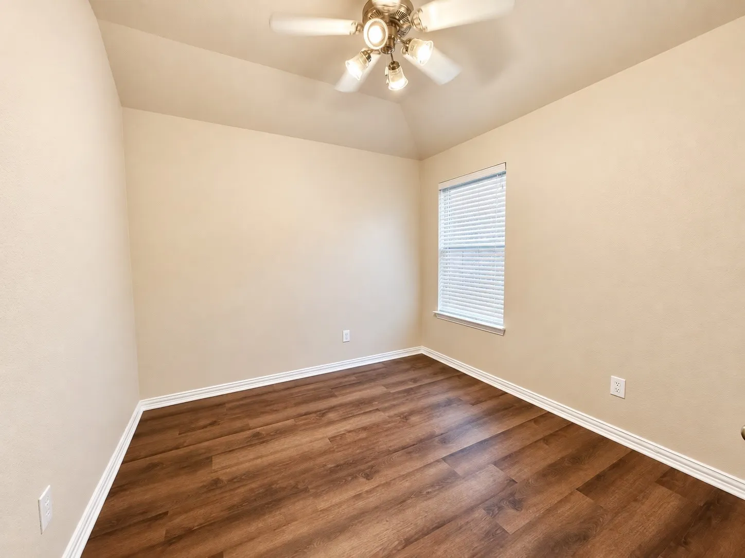 Wood-finish flooring, vaulted ceiling, ceiling fan with light fixture, window with blinds, and neutral wall tones