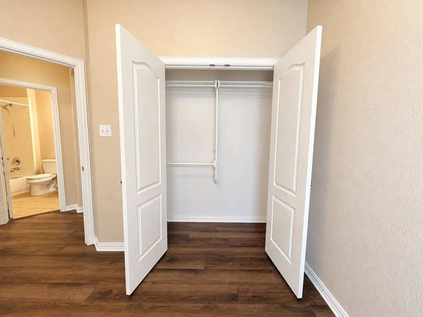 Wood-finish flooring throughout, providing access to a closet with dual hanging rods and panel doors, and a full bathroom featuring a tub with shower
