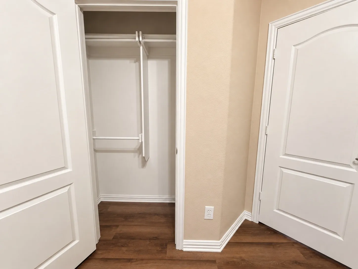Wood-finish flooring, white paneled doors, and a built-in closet with shelving and hanging rods