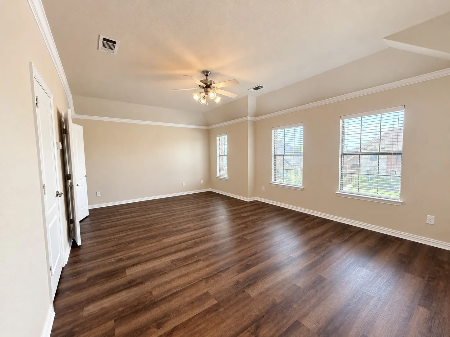 Spacious room featuring wood-finish flooring, multiple windows with blinds, a tray ceiling, and a ceiling fan with integrated lighting