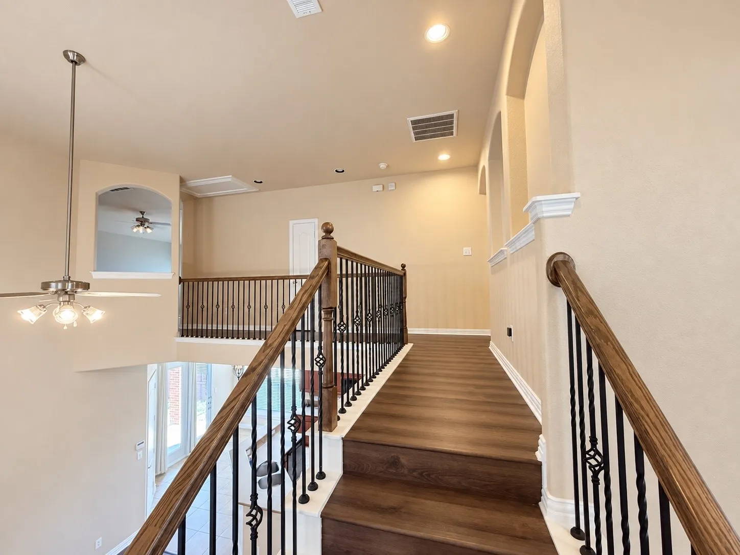 Staircase featuring wood-finish treads and handrail, wrought iron balusters, recessed lighting, and an arched wall opening