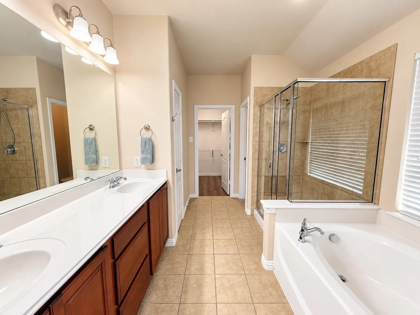 Dual vanity with integrated sinks, wood-finish cabinetry, tile flooring, separate shower with glass enclosure, and built-in tub