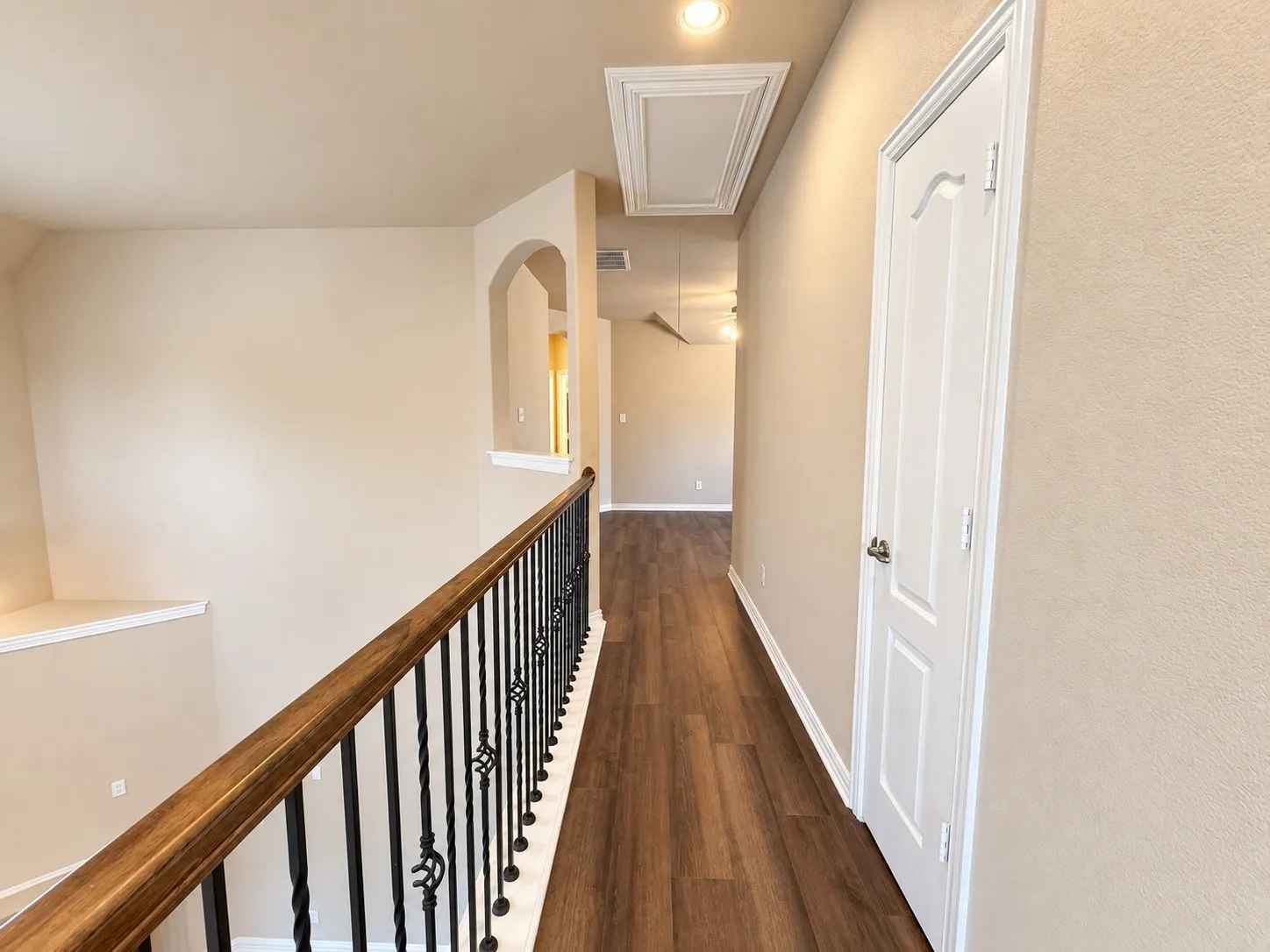 Wood-finish flooring throughout the hallway, decorative wrought iron balusters, and a light-toned interior paint finish