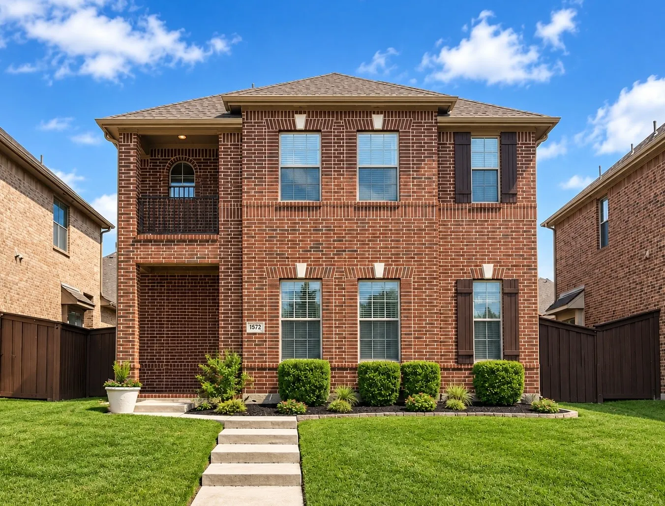 Brick exterior with a covered entry, second-story balcony with metal railing, and decorative window shutters