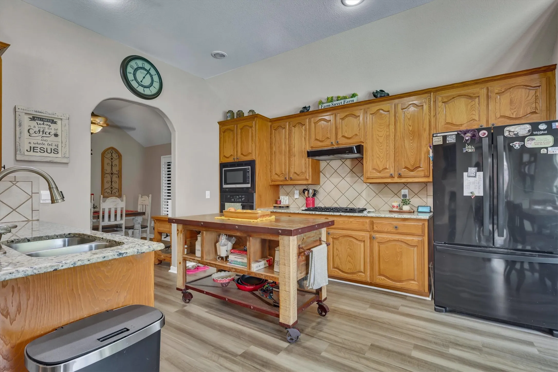 Kitchen featuring wood-finish cabinetry, granite-style countertops, a stainless steel sink with a gooseneck faucet, a tile backsplash, and a built-in microwave