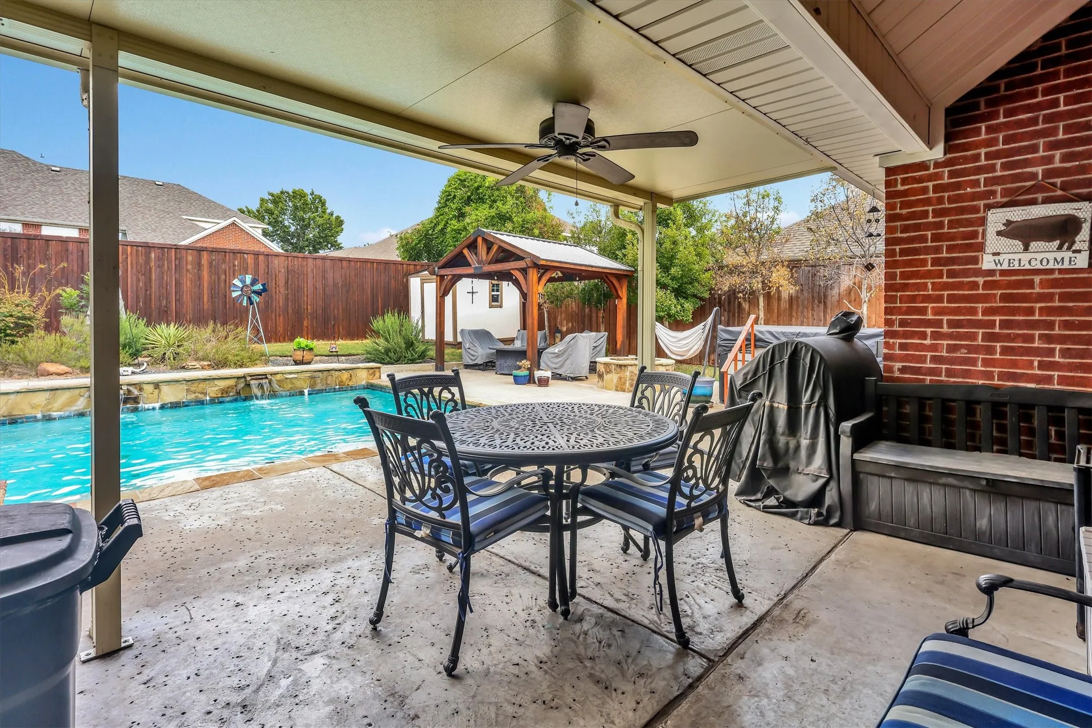 Covered patio with an outdoor ceiling fan, brick wall accent, and a built-in bench