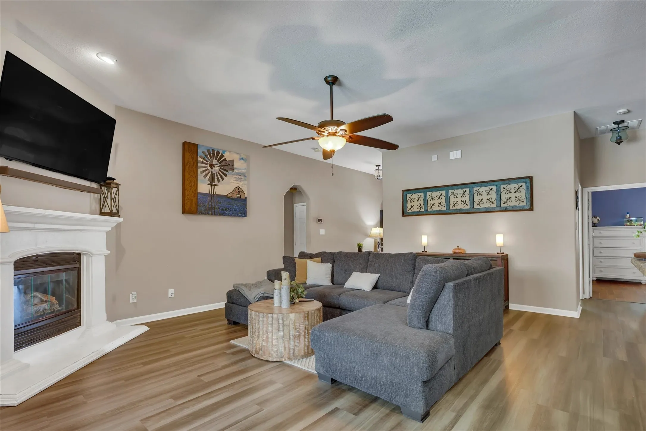 Living area featuring wood-finish flooring, a fireplace with a white mantel, a ceiling fan with integrated lighting, and recessed ceiling lights