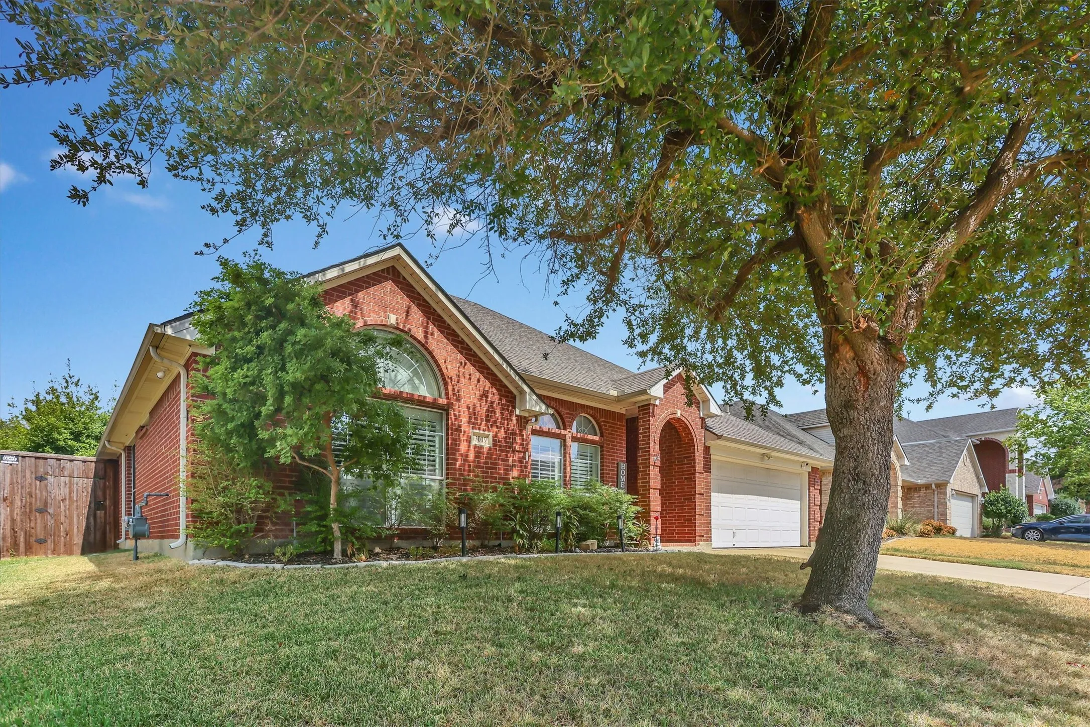 Red brick exterior with white trim, arched window, attached garage, and mature landscaping