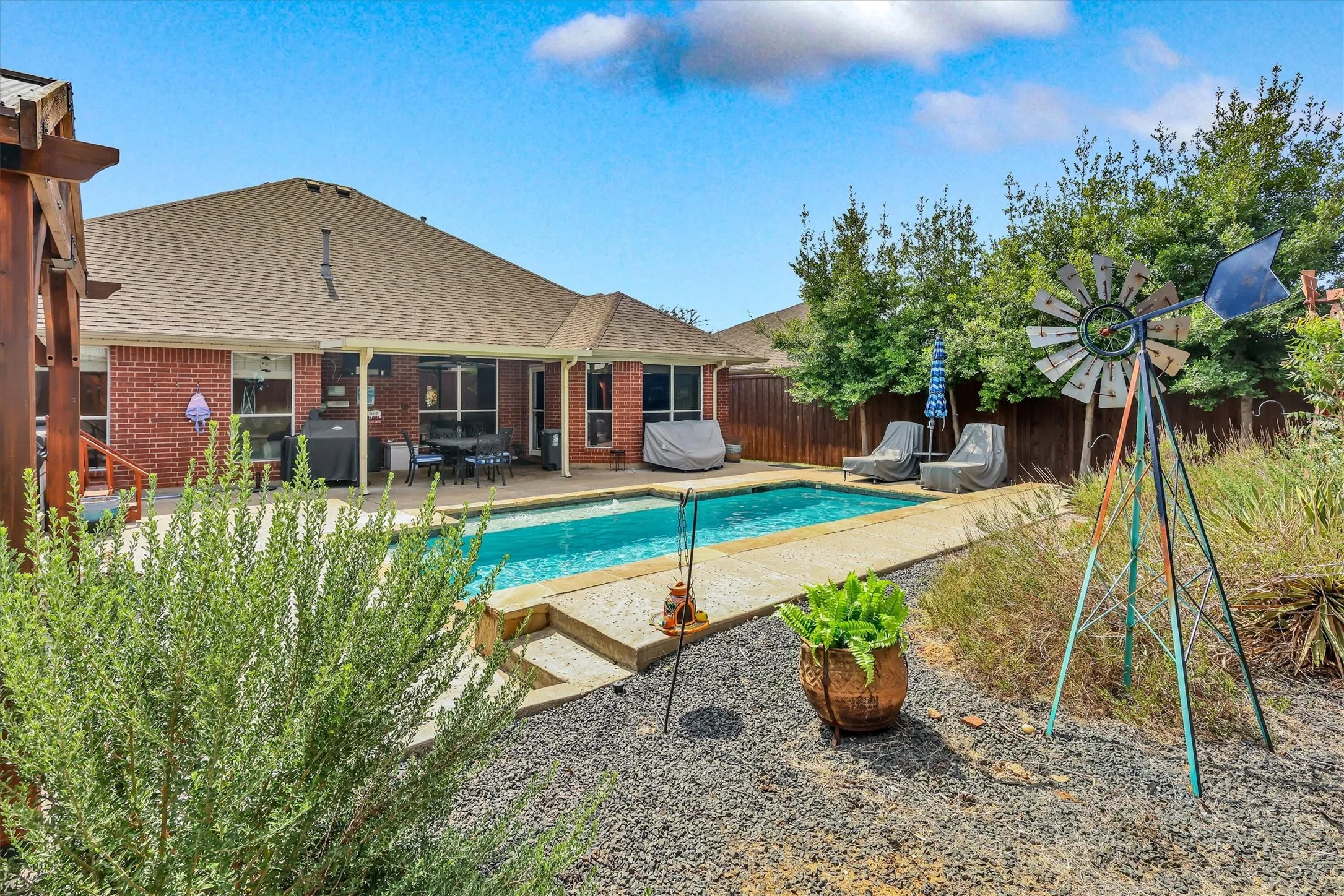 Brick exterior with a covered patio, inground pool, and surrounding concrete decking