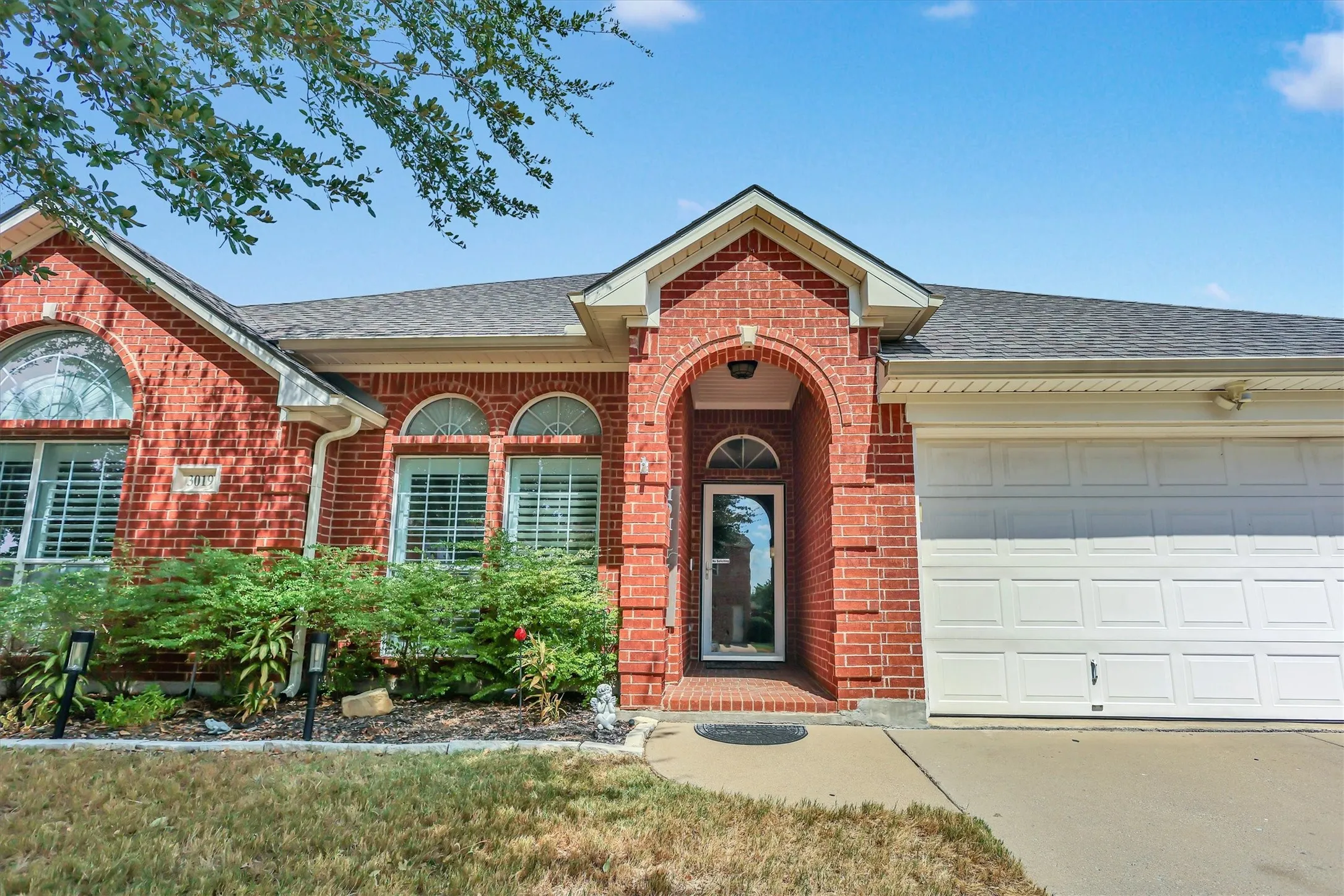 Brick exterior with an arched entry, white garage door, and a shingled roof