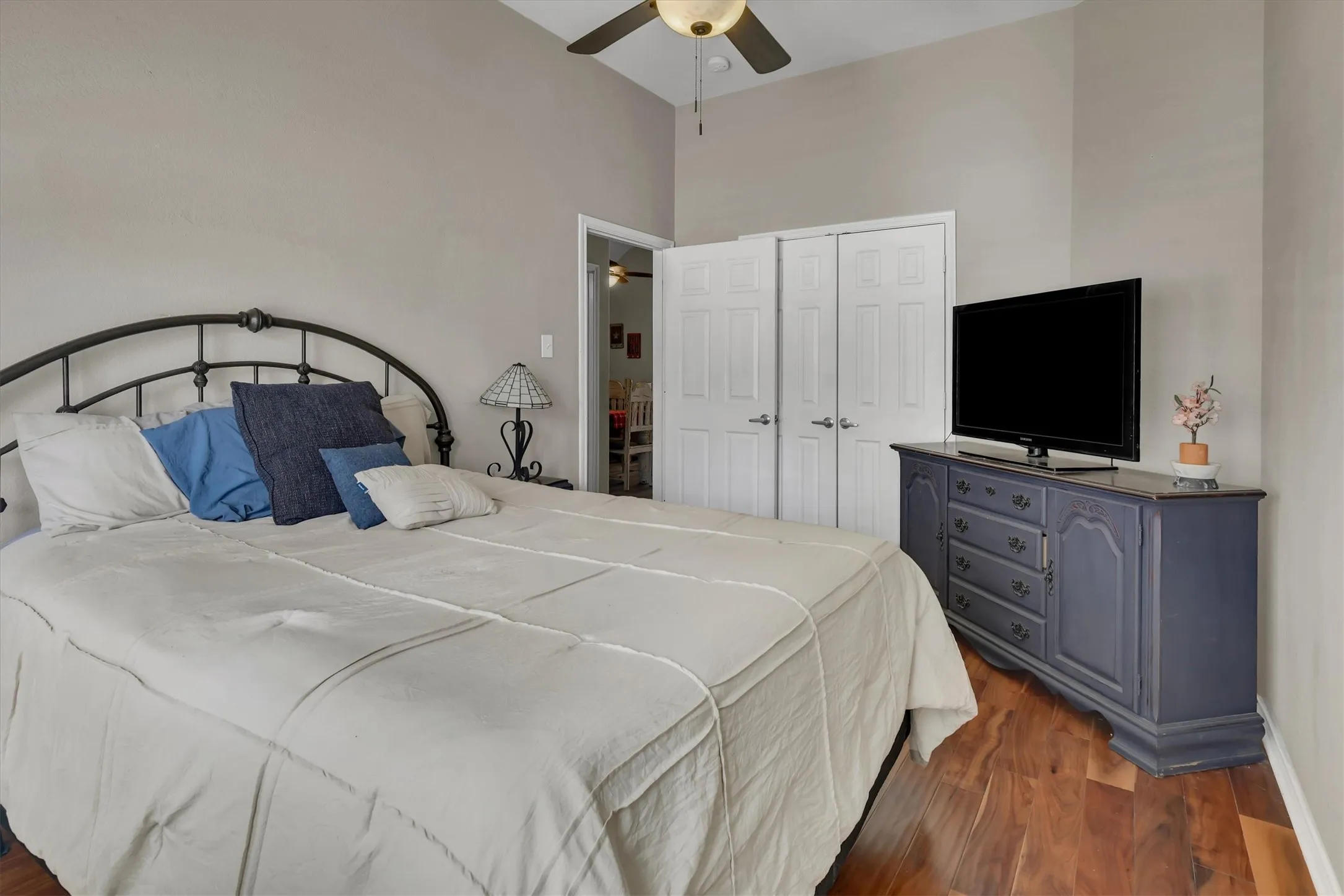 Vaulted ceiling, ceiling fan with light fixture, wood-finish flooring, and white bifold closet doors