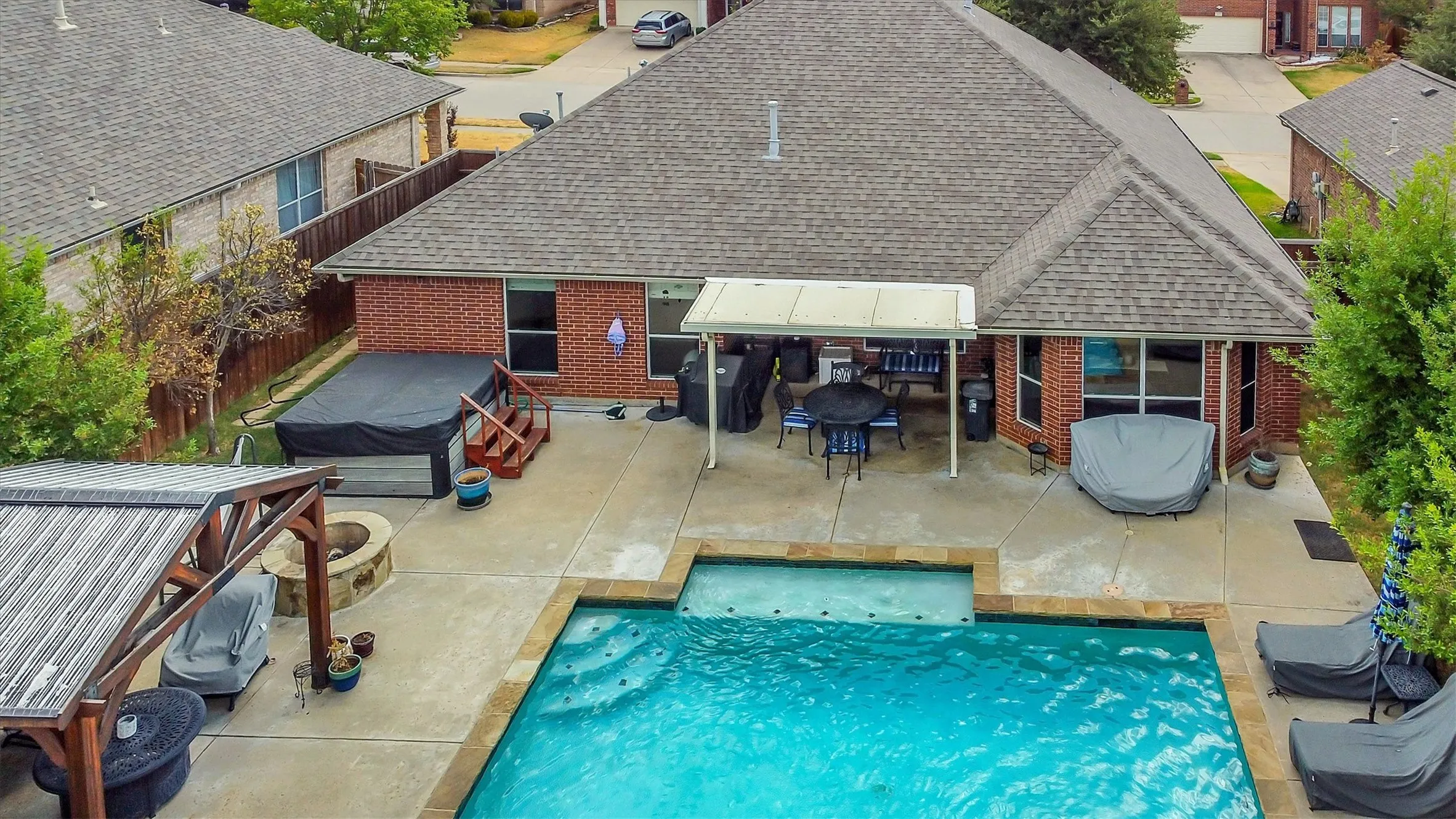 Expansive backyard featuring a rectangular swimming pool, integrated spa, covered patio, and a stone fire pit