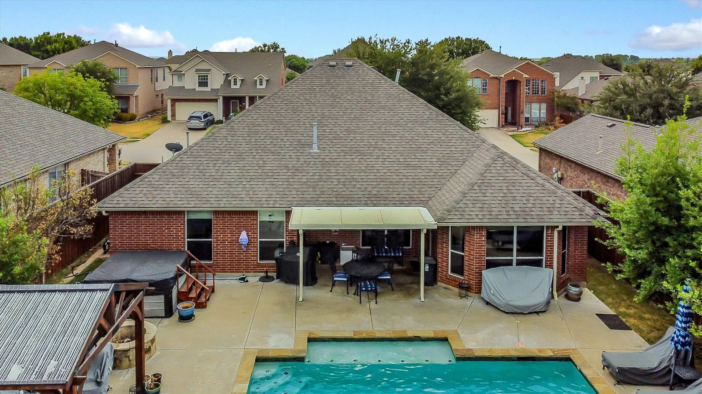 Expansive concrete patio with an in-ground swimming pool, covered outdoor dining area, and a built-in outdoor spa