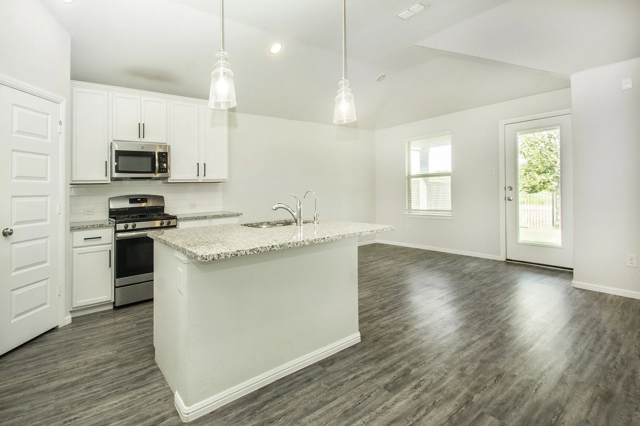 Kitchen featuring vaulted ceiling, stainless steel appliances, backsplash, a kitchen island with sink, and white cabinets