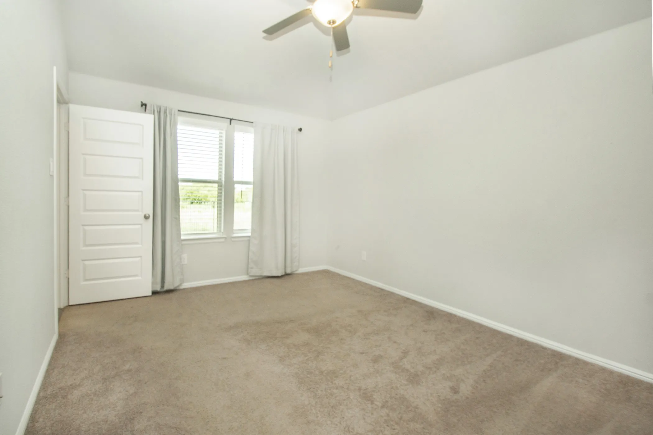Carpeted spare room featuring ceiling fan and baseboards