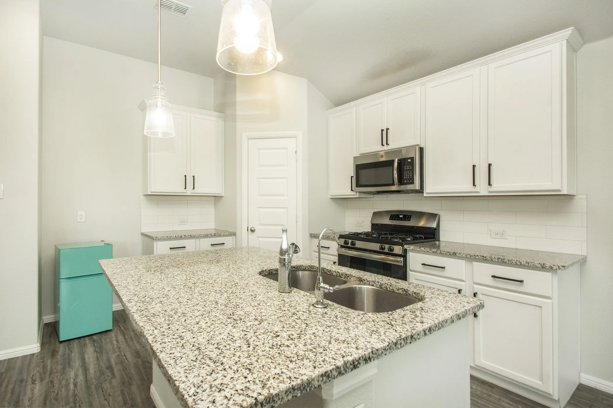 Kitchen featuring stainless steel appliances, decorative backsplash, dark wood-type flooring, and white cabinets